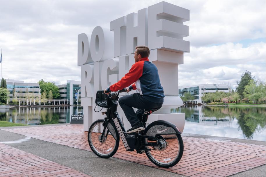 A person rides a bicycle near a large sculpture that says DO THE RIGHT THING beside a body of water