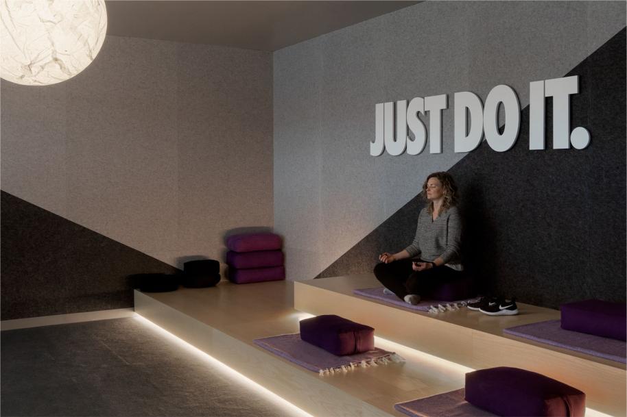 A meditation room with a person sitting cross-legged on a wooden bench beneath the words just do it